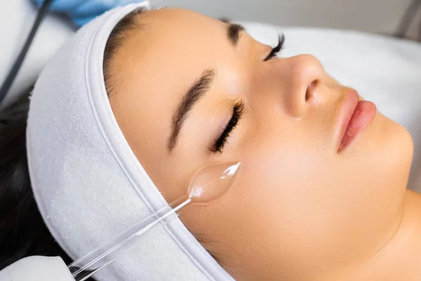 Hardware vacuum facial massage for skin smoothness. Woman enjoys procedure expecting quality improvement. Monitoring expert workflow