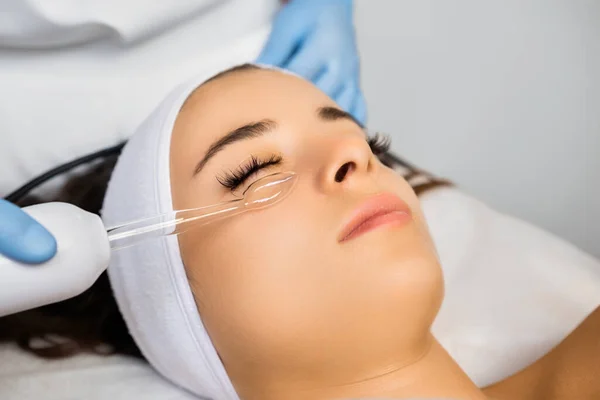 Hardware vacuum facial massage for skin smoothness. Woman enjoys procedure expecting quality improvement. Monitoring expert workflow