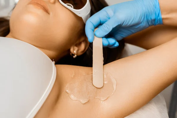 Wax depilation of armpit in a beauty salon for young woman.
