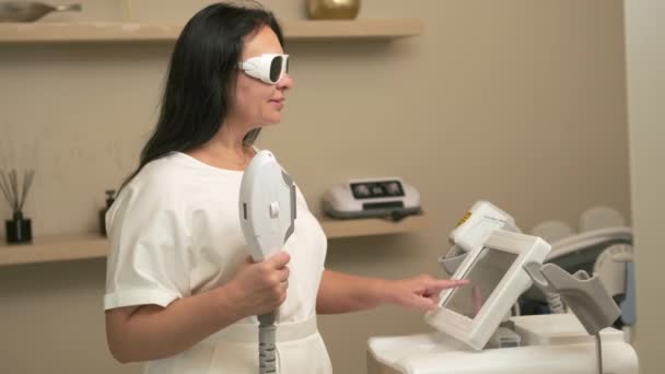 戴防护护目镜的深色头发皮肤科医生操作激光脱毛机 美容师在办公室准备激光脱毛 — 图库视频影像