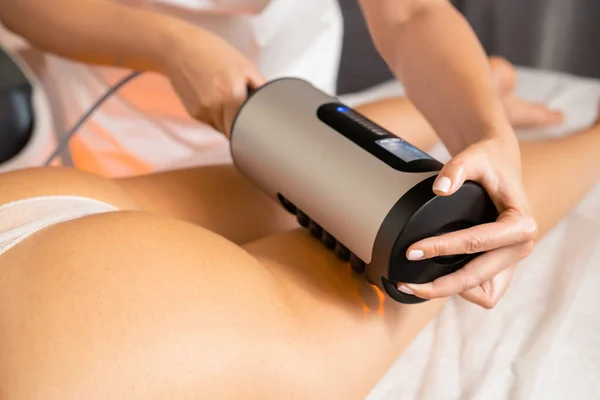 Vibrational anti-cellulite therapy massage device for figure correction in spa salon. Professional cosmetologist works with woman figure correction