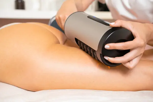 stock image Electric massage device for figure correction in clinic room. Beautician doing massage of clients hip thigh and legs with vibrational therapy apparatus