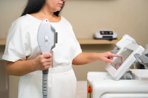 Dermatologist stands with equipment of laser hair removal device. Cosmetologist adjusts device settings for laser hair removal procedure