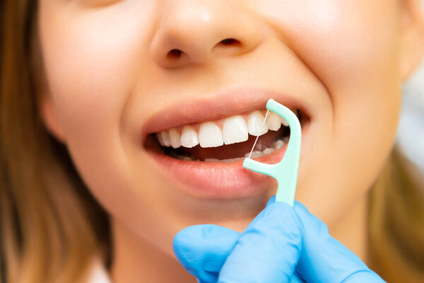 Close up woman teeth with dental floss, Doctor in rubber gloves shows how to do dental care.
