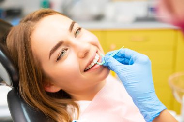 Bir dişçi, dişçi muayenehanesinde genç bir bayana diş ipi kullanımında rehberlik eder..