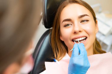 Diş hekimi, dişçi kliniğindeki genç bir kadına uygun diş ipi kullanımını gösteriyor.