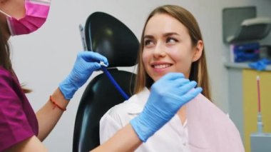 Özel bir klinikte dişçiyle dişçi randevusuna hazırlanan kahverengi saçlı genç bir kadın. Kadın dişleri tedavi etmek ve hatta gülümsemek istiyor.