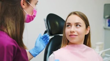 Özel diş hekimliği randevusunda diş beyazlatma prosedürü sona erdi. Diş hekimi, beyazlatma prosedürlerinden sonra kadın hastalara tavsiye veriyor