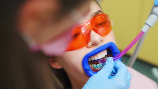 液体吸引のための管が付いている紫外線からの保護眼鏡の患者 歯科医は 歯とキャビティ治療に取り組むために女性の口にチューブを置きます — ストック動画