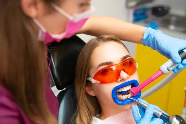 Dentist performs professional teeth cleaning for female patient at the dental office