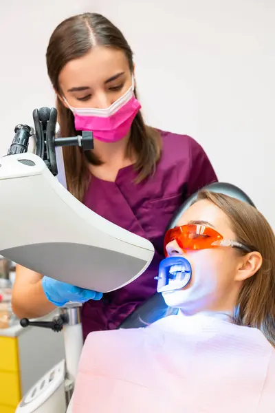 Młody Dentysta Masce Twarzy Wykonuje Wybielanie Zębów Przy Użyciu Lampy — Zdjęcie stockowe