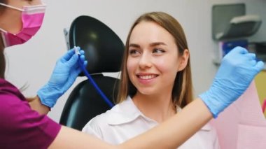 Kahverengi saçlı kadın özel klinikte dişçi muayenesine hazırlanıyor. Sandalyede oturan hasta dişlek bir gülümsemeye sahip olmak istiyor.