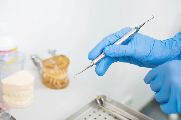 A dentists hands holding dental instruments for teeth treatment, with jaw models in the background.