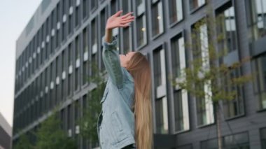 Mutlu genç bir kadın kollarını havaya kaldırarak etrafında dönüyor. Neşeli, gevşemiş bayan ofis binasına karşı bitirilen iş gününden memnun.