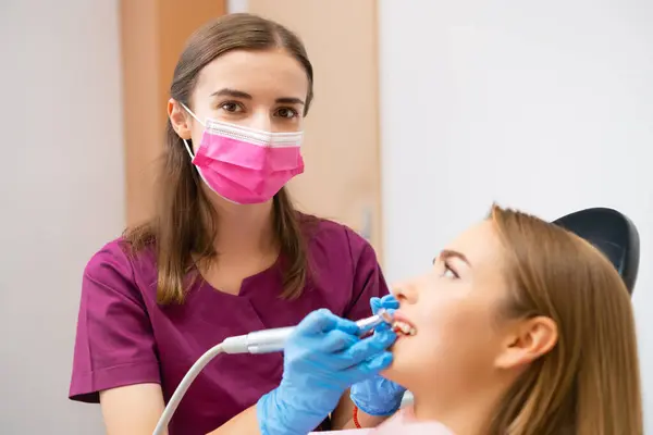 A dentist is performing a teeth grinding procedure on a lovely woman to enhance her smile.