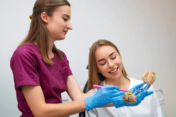 A dental hygienist provides a practical demonstration to a young woman on the proper technique for cleaning teeth