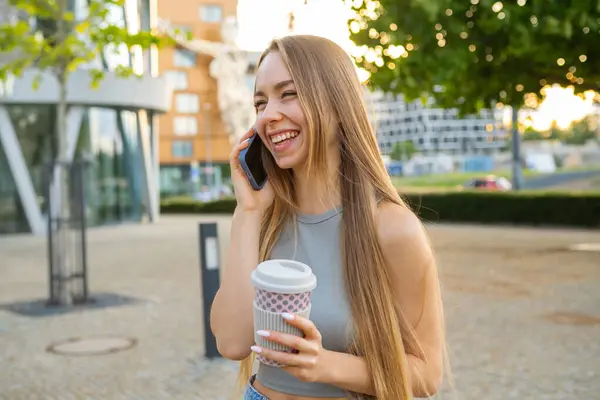 Rahat bayan sıcak kahve içiyor ve telefonda erkek arkadaşıyla konuşuyor. Genç kadın gülüyor. Yaz kenti parkında erkek arkadaşını arıyor.