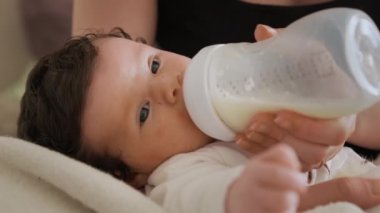 Annenin ellerinde yatan yeni doğmuş bebek şişeden süt yiyor. Kadın şişeyi dikkatlice tutuyor ve kızının yeterince beslenmesini sağlıyor.