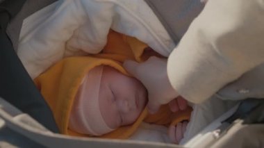 Anne eli, bebek arabasında uyuyan parlak çocuk kıyafetlerini ayarlıyor. Kadın bebeğin dışarıda sıcak ve rahat hissetmesini sağlar.