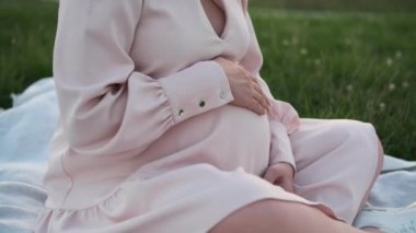 Genç hamile anne, çimenli tarlaya yayılmış battaniyede otururken şefkatle koca göbeğini okşar. Kadın, bebek bedeninin dokunuşlarını hisseder.