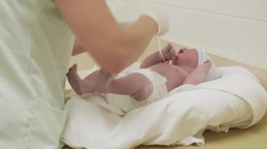 Hastanede lastik eldivenli hemşire yeni doğan bebeğe dikkatlice etiket yapıştırıyor. Şapkalı bebek yuvarlak yatakta yatar ve çevresindeki ani değişimden dolayı ağlar.
