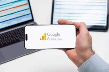 Google Analitik logosu, arka planda grafiksel diyagramlı tablet ve dizüstü bilgisayarlı akıllı telefonun ekranında, Aralık 2023, Prag, Çek Cumhuriyeti.