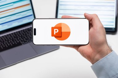 Powerpoint logosu, bilgisayarlı akıllı telefonun ekranında ve arka planda grafiksel şemalar olan tablet, Aralık 2023, Prag, Çek Cumhuriyeti.