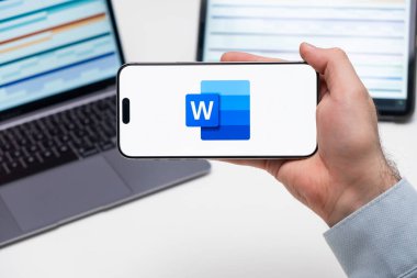 Kelime logosu, arka planda grafiksel diyagramlı tablet ve dizüstü bilgisayarlı bir akıllı telefonun ekranında, Aralık 2023, Prag, Çek Cumhuriyeti.