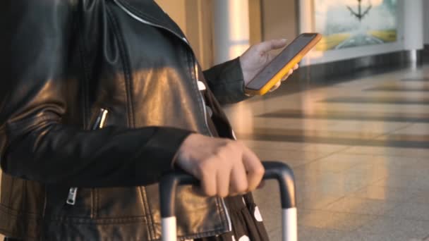 Siyah Ceketli Bir Kadın Havaalanında Elinde Bavuluyla Akıllı Telefonunu Kontrol — Stok video