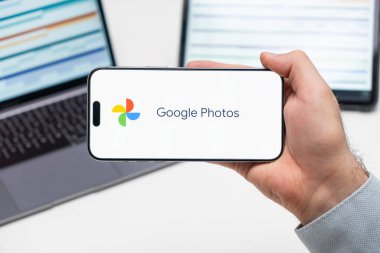 Bilgisayarın ve tabletin önündeki adamın cep telefonu ekranındaki uygulamanın Google Fotoğrafları logosu, Aralık 2023, Prag, Çek Cumhuriyeti