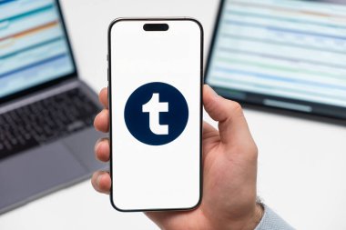 Sosyal medya uygulamalarının Timblr logosu erkeğin elindeki akıllı telefon ekranında, laptopta ve tablette arka planda, Aralık 2023, Prag, Çek Cumhuriyeti