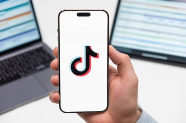 Sosyal medya uygulamalarının Tiktok logosu erkeğin elindeki akıllı telefon ekranında, laptopta ve tablette arka planda, Aralık 2023, Prag, Çek Cumhuriyeti