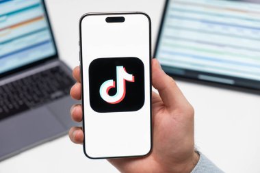 TikTok sosyal medya uygulamalarının logosu erkek eli ekranında, dizüstü bilgisayar ve tablet arka planda.