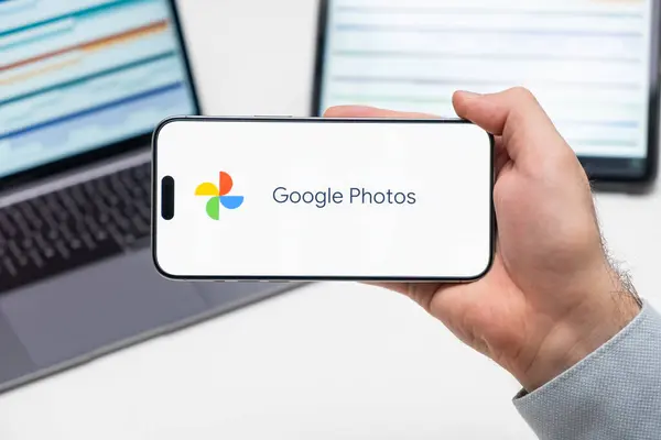 ラップトップとタブレットの前に男性が保有する携帯電話の画面上のGoogleの写真ロゴ 2023年12月 プラハ チェコ ストック画像