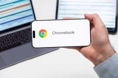 Akıllı telefon ekranındaki Chromebook uygulama logosu Man 's Hand, laptop ve tablet arka plandaki masada, Aralık 2023, Prag, Çek Cumhuriyeti.