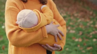 Anne, temiz havada oynadıktan sonra huzur içinde dinlenmek için kucağında bebek beşiği taşıyor. Sarı kazaklı kadın parkta doğayı sevmeyi öğretiyor.