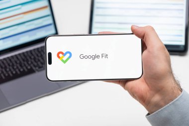 Bilgisayarın ve tabletin önündeki adamın cep telefonu ekranındaki uygulamanın Google Fit logosu, Aralık 2023, Prag, Çek Cumhuriyeti