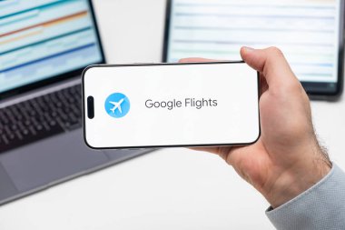Google Uçuşları uygulama logosu erkek eli, laptop ve tablet akıllı telefon ekranında arka planda, Aralık 2023, Prag, Çek Cumhuriyeti.