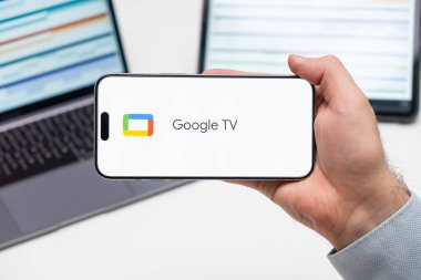 Bilgisayarın ve tabletin önünde bulunan adamın cep telefonu ekranındaki uygulamanın Google TV logosu, Aralık 2023, Prag, Çek Cumhuriyeti
