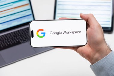 Google Workspace uygulama logosu erkek eli, dizüstü bilgisayar ve tablet ekranında arka plandaki masada, Aralık 2023, Prag, Çek Cumhuriyeti.