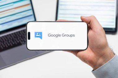 Google Groups uygulamasının logosu bilgisayarın ve tabletin önünde bulunan adamın cep telefonu ekranında, Aralık 2023, Prag, Çek Cumhuriyeti