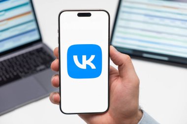 Sosyal medya uygulamalarının VK logosu arka planda erkek eli, dizüstü bilgisayar ve tablet akıllı telefon ekranında