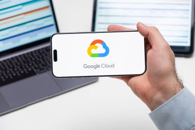 Bilgisayarın ve tabletin önündeki adamın cep telefonu ekranında uygulamanın Google Bulutu logosu, Aralık 2023, Prag, Çek Cumhuriyeti