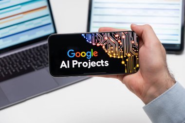 Google AI, cep telefonu ekranındaki uygulama logosunu laptopun ve tabletin önündeki adamın elinde tutuyor, Aralık 2023, Prag, Çek Cumhuriyeti
