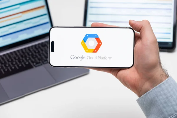 stock image Google Cloud Platform logo of app on the screen of mobile phone held by man in front of the laptop and tablet, December 2023, Prague, Czech Republic