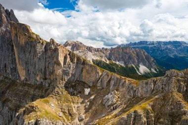 Steep slopes of Seceda mountain overgrown with grass on sunny summer day. Giant rocky ridgeline in Alps under cloudy sky aerial view