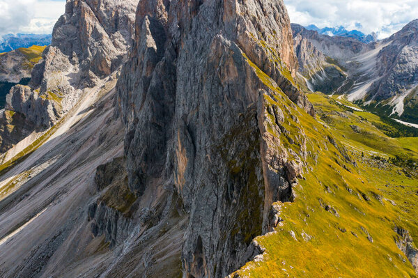Rocky Seceda mountain range slope covered with fresh green grass in shadow. Scenic wild nature of Italian Alps on sunny summer day aerial view