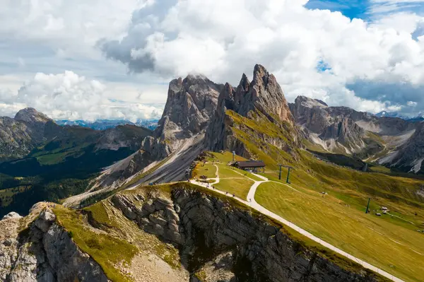 Tourist observation point overlooking Seceda ridgeline stretching in Italian Alps. Giant rocky mountain range against cloudy sky aerial view