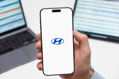 PRAG, CZECHIA - Şubat 2024: Hyundai otomobil logosu, arka planda erkek eli ve dizüstü bilgisayarda akıllı telefon ekranında 