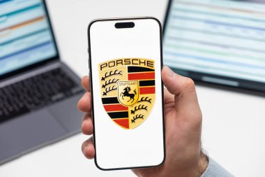 PRAG, CZECHIA - Şubat 2024: Porsche otomobil logosu arka planda erkek eli ve dizüstü bilgisayarda akıllı telefon ekranında 